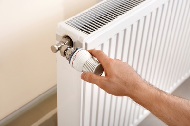 Man adjusting heating radiator thermostat indoors