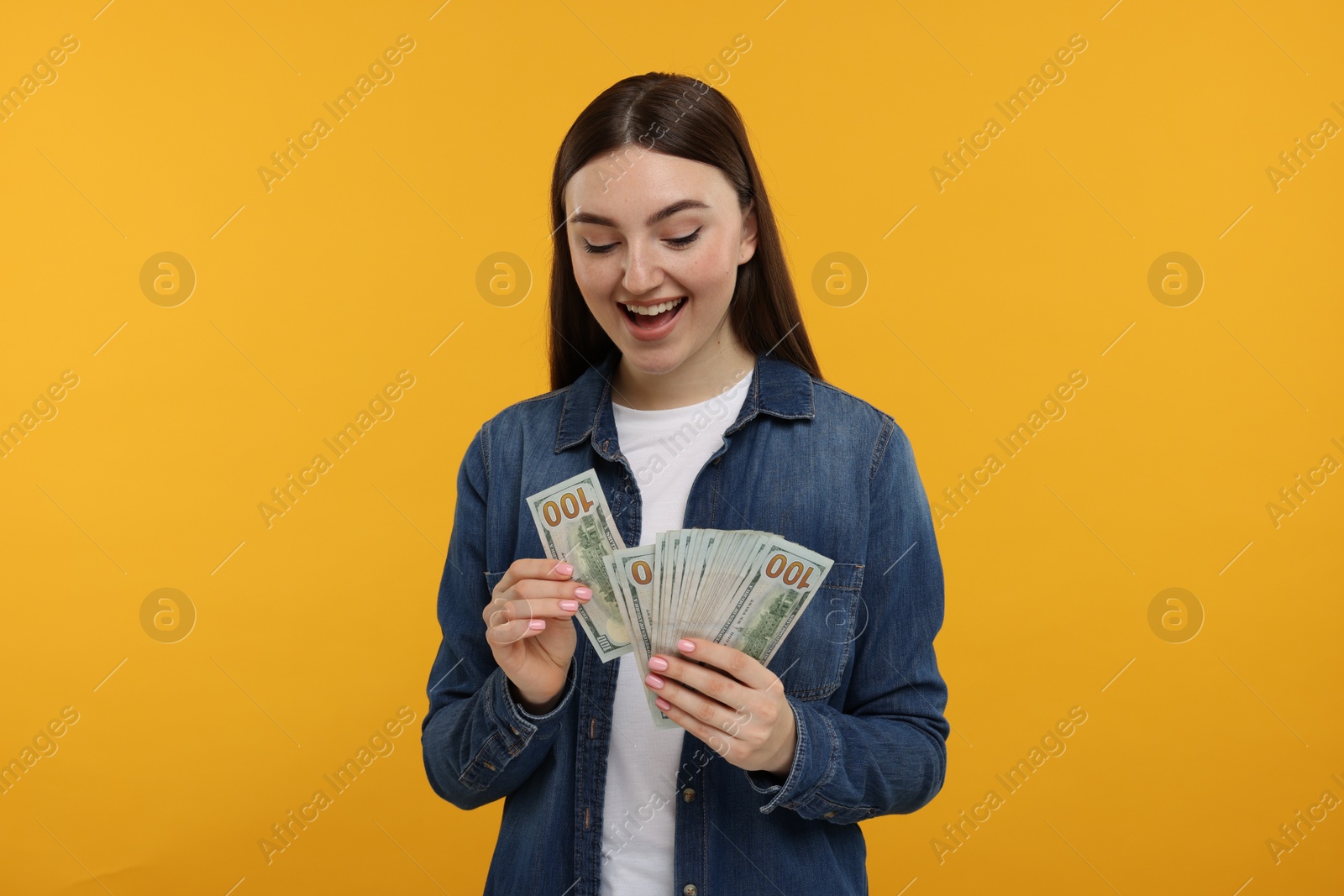 Photo of Happy woman with dollar banknotes on orange background