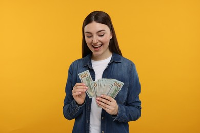 Happy woman with dollar banknotes on orange background