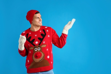 Photo of Man in Christmas sweater, mittens and hat on blue background, space for text