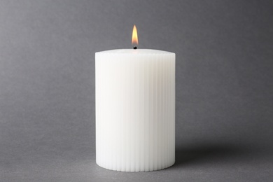 Stylish white burning candle on grey background