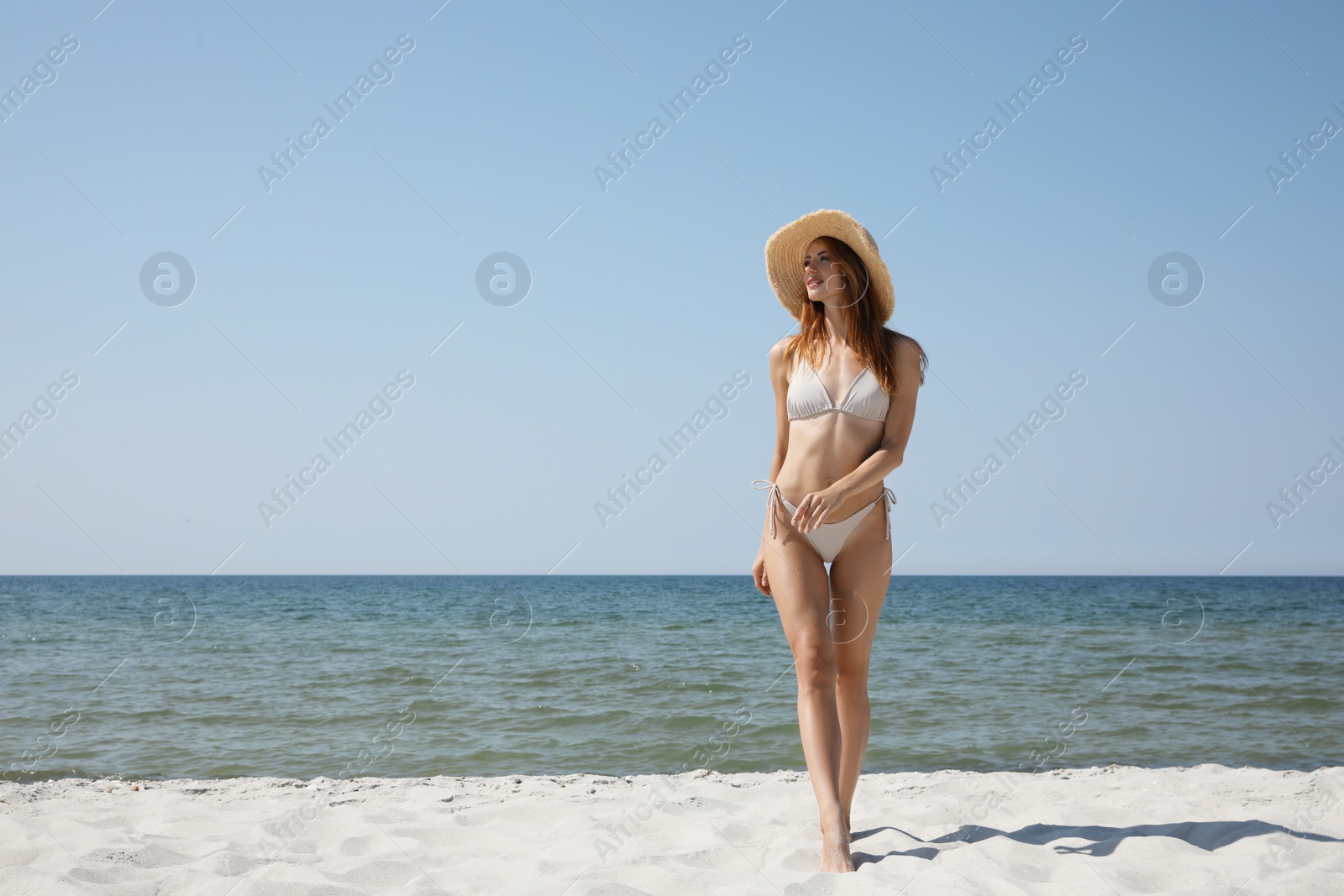 Photo of Attractive woman in bikini walking on sandy beach near sea