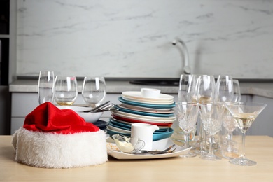 Photo of Santa hat and dirty dishware on wooden table in kitchen after party