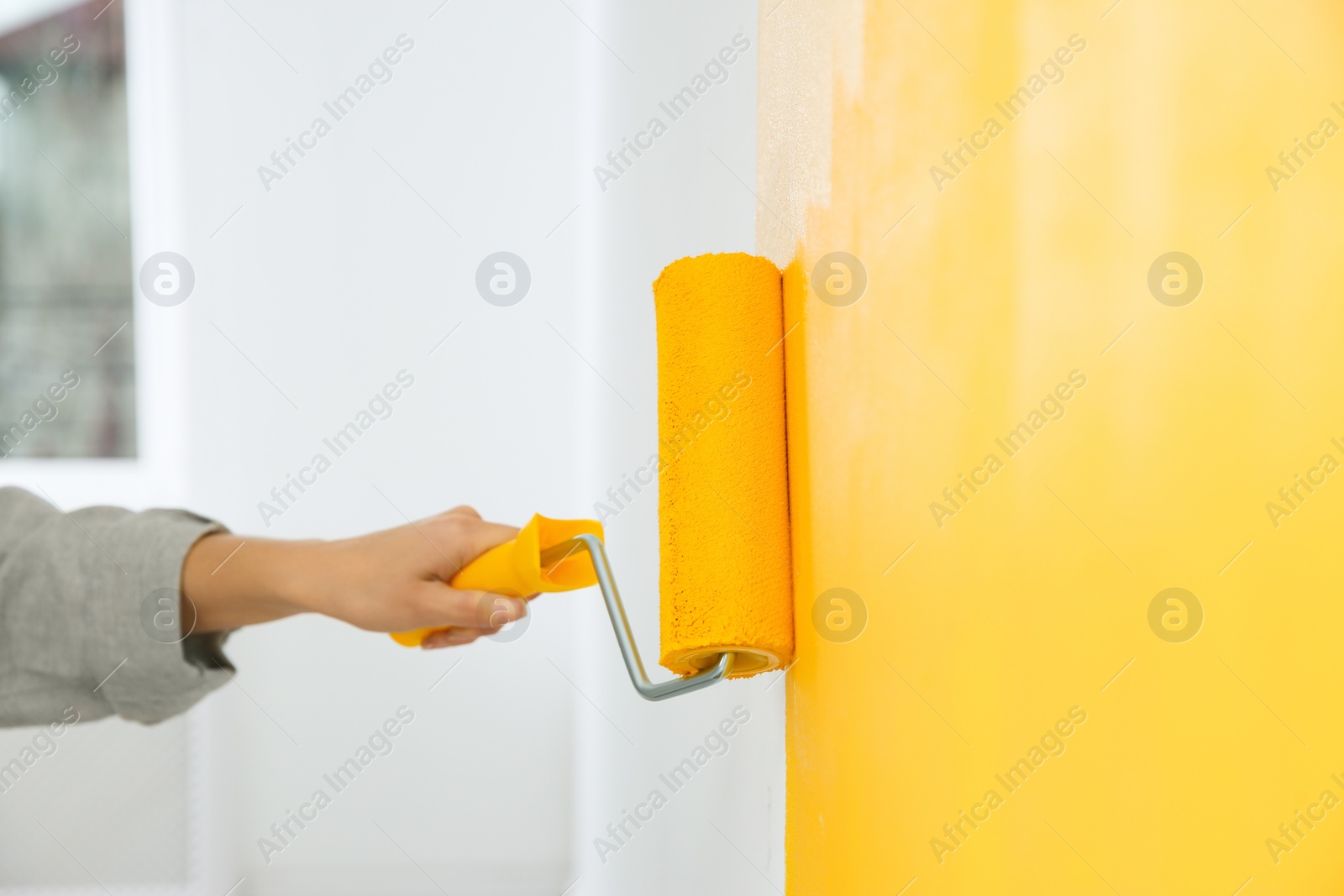 Photo of Woman painting white wall with yellow dye, closeup. Interior renovation