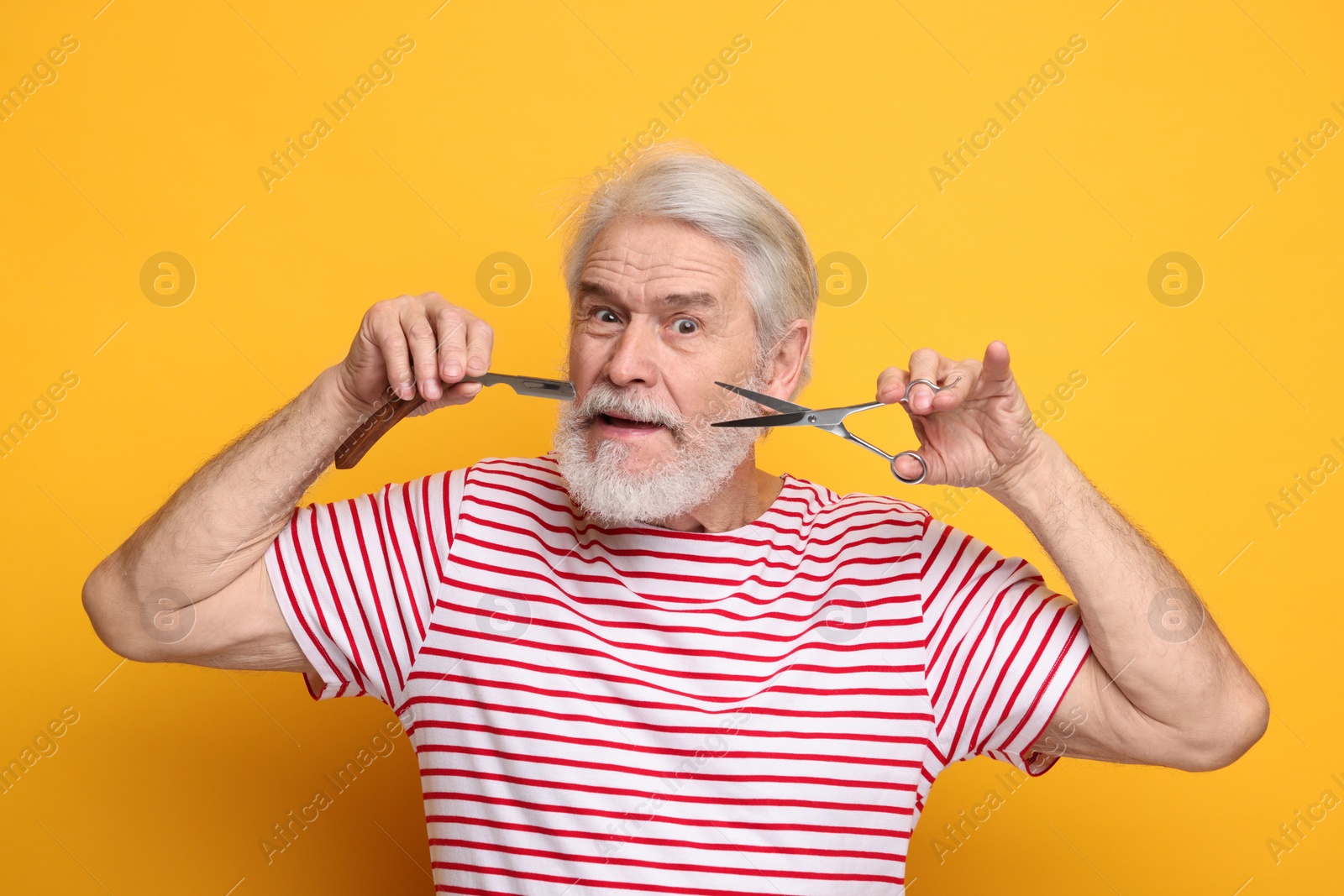 Photo of Senior man with mustache holding scissors and blade on orange background