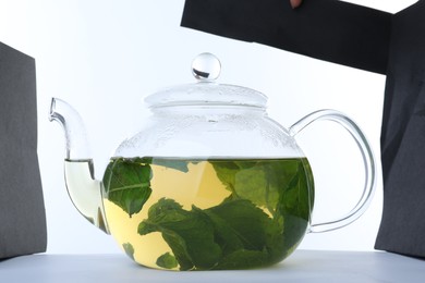 Photo of Teapot with hot aromatic mint tea isolated on white