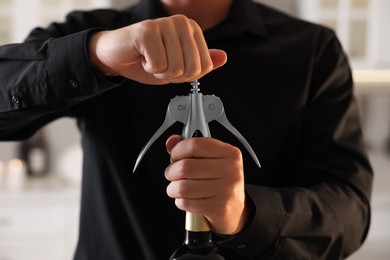 Photo of Man opening wine bottle with corkscrew indoors, closeup