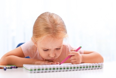 Upset little left-handed girl drawing at table in room