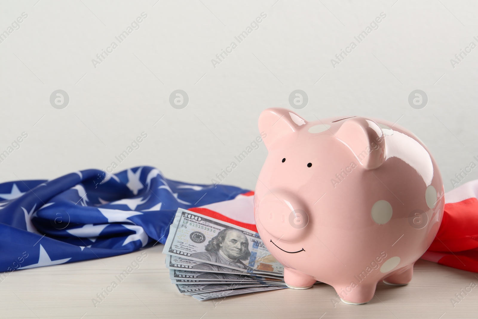 Photo of Piggy bank, American flag and dollar banknotes on white wooden table