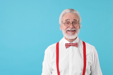 Photo of Portrait of stylish grandpa with glasses and bowtie on light blue background, space for text