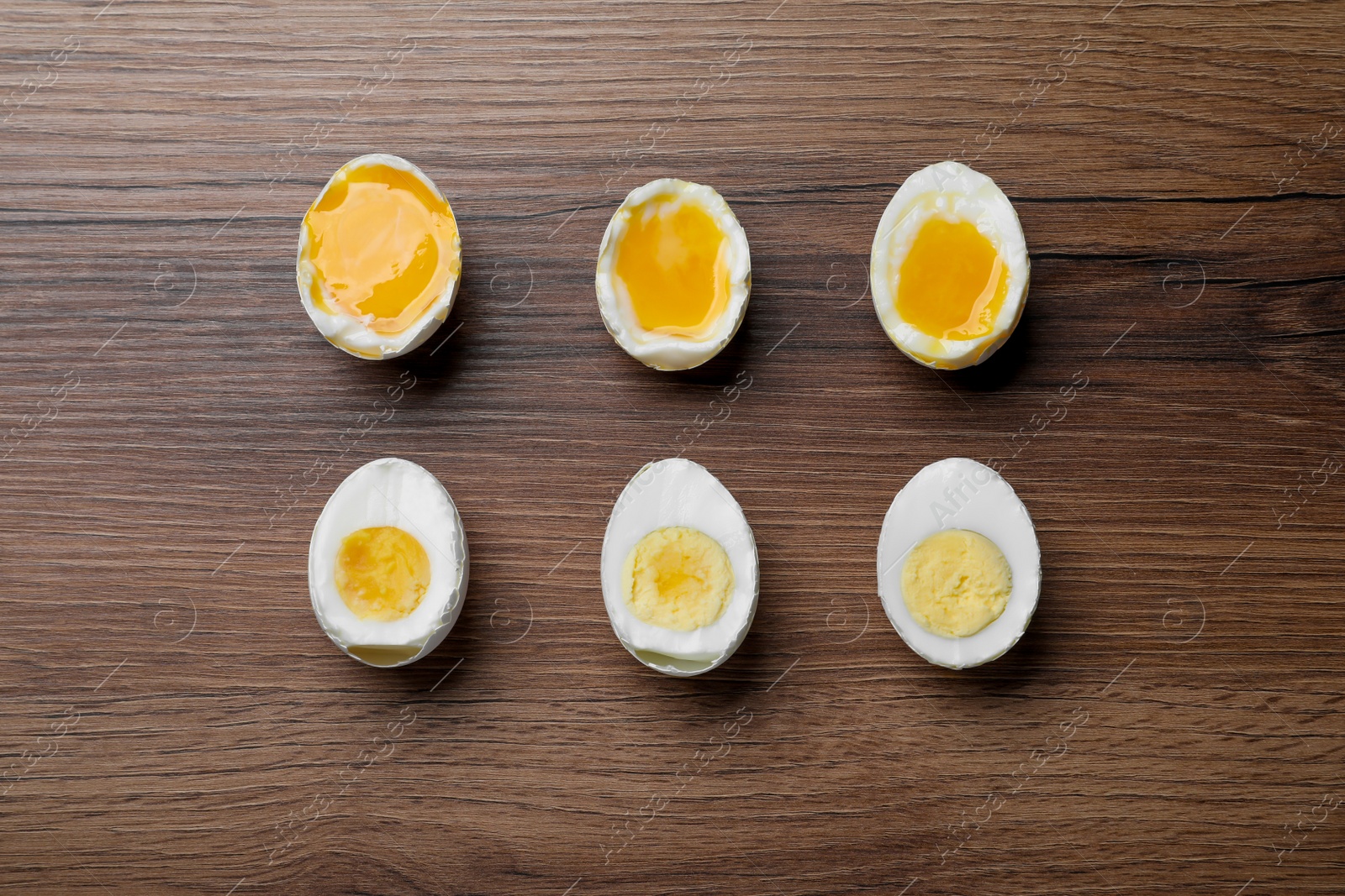 Photo of Different readiness stages of boiled chicken eggs on wooden table, flat lay