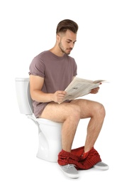 Young man reading newspaper while sitting on toilet bowl. Isolated on white