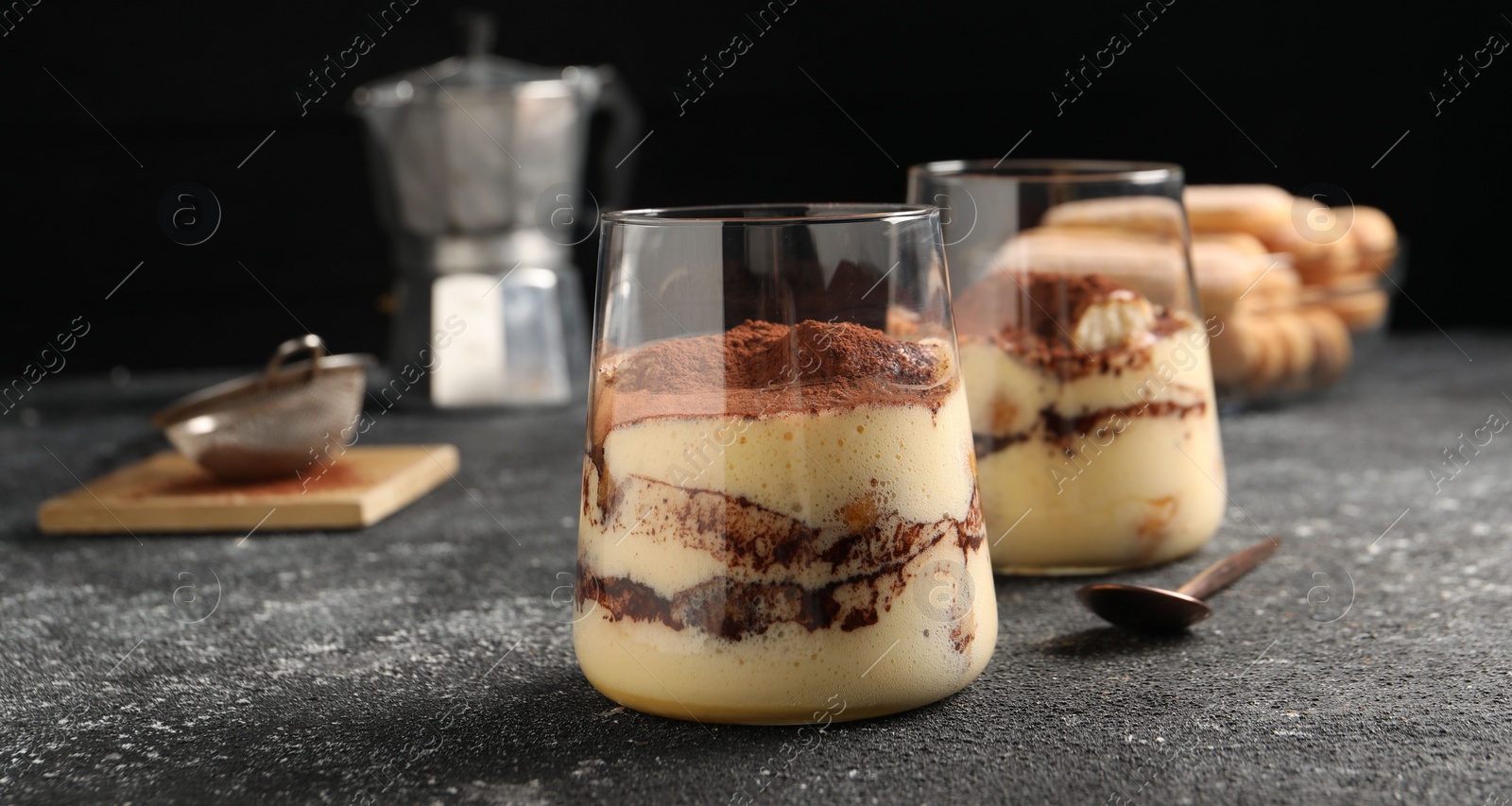 Photo of Delicious tiramisu in glasses on grey textured table, closeup