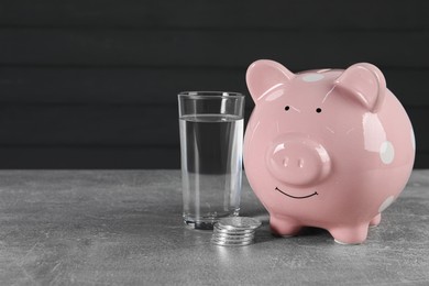 Photo of Water scarcity concept. Piggy bank, coins and glass of drink on grey table, space for text