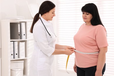 Photo of Nutritionist measuring overweight woman's waist with tape in clinic