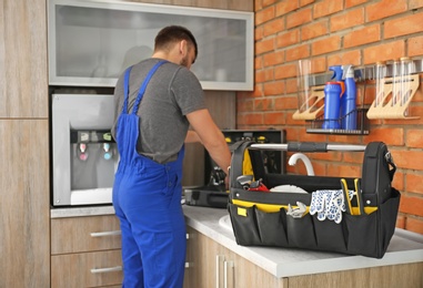 Set of professional tools and plumber in uniform indoors