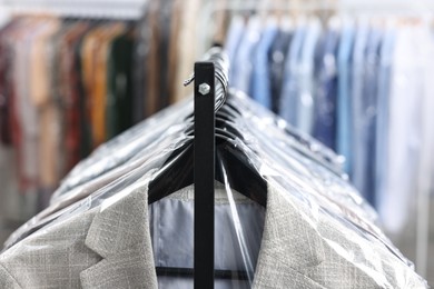 Photo of Dry-cleaning service. Many different clothes in plastic bags hanging on rack indoors, closeup