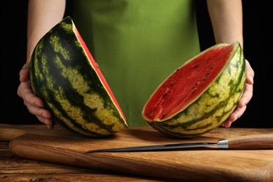 Photo of Woman with delicious halved watermelon at wooden table against black background, closeup