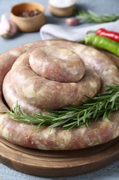 Photo of Homemade sausages and rosemary on light grey wooden table, closeup