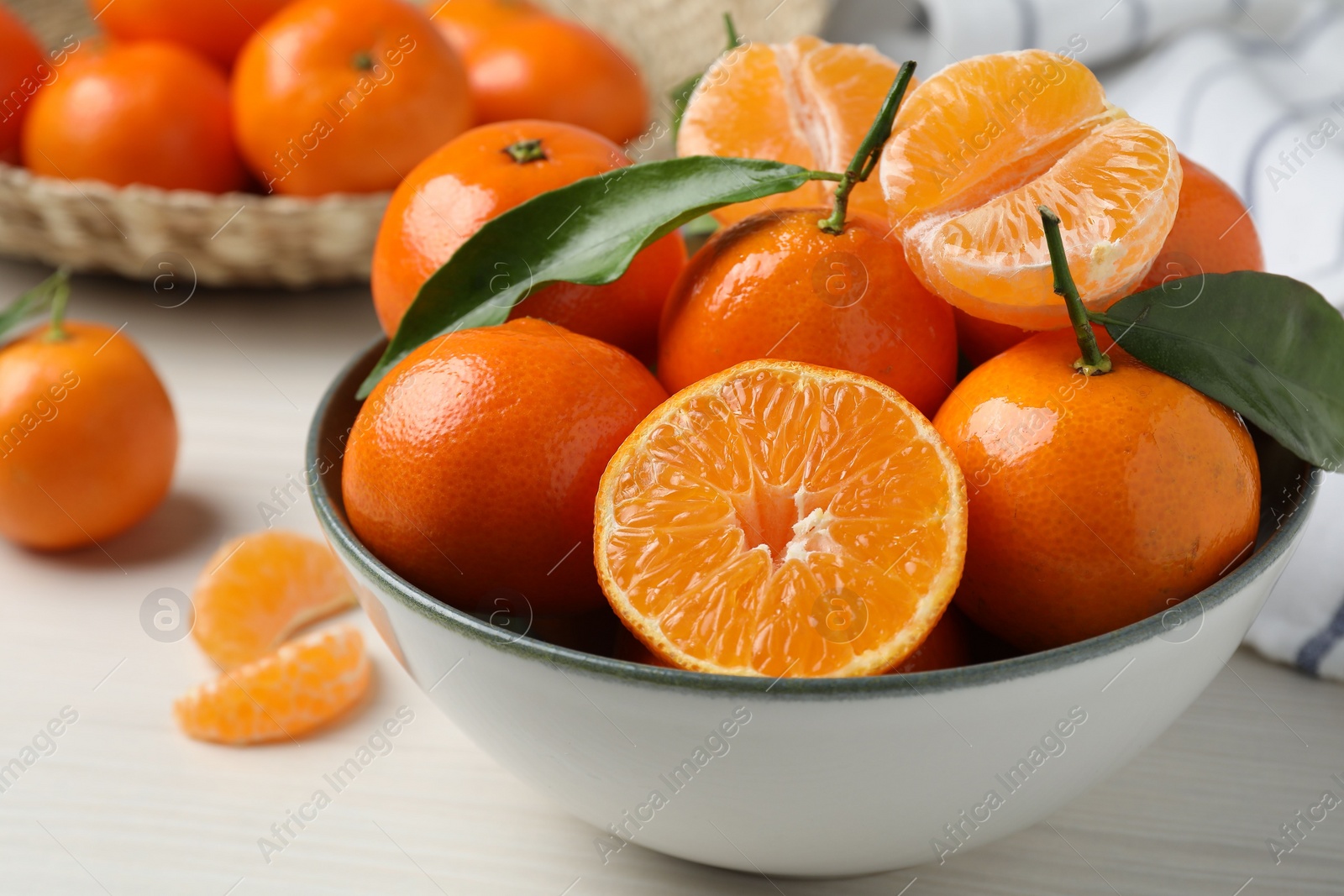 Photo of Delicious tangerines with green leaves in bowl on white wooden table, closeup