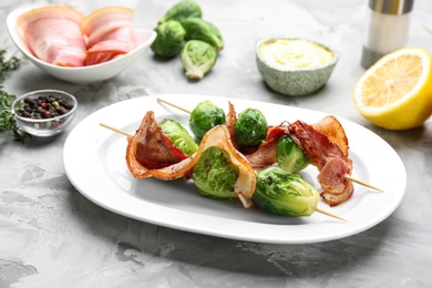 Photo of Skewers with Brussels sprouts and bacon in plate on grey table