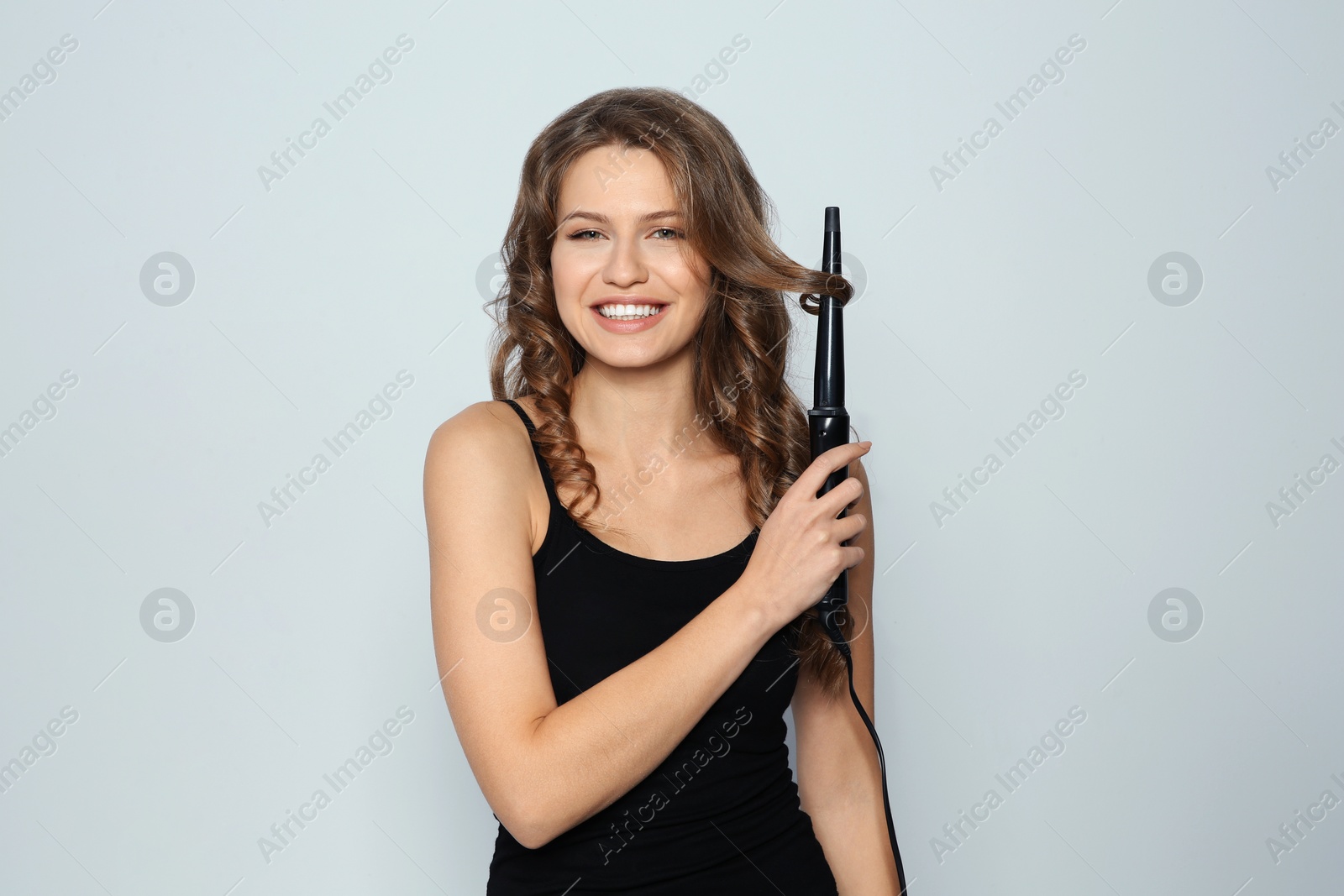 Photo of Portrait of young woman with shiny wavy hair using curling iron on color background