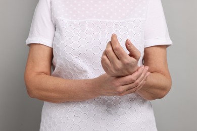 Arthritis symptoms. Woman suffering from pain in wrist on gray background, closeup