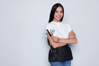 Photo of Portrait of happy hairdresser with professional scissors and comb on light background, space for text