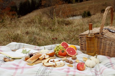 Photo of Blanket with picnic basket, wine, snacks and book outdoors on autumn day. Space for text