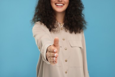 Photo of Woman welcoming and offering handshake on light blue background, closeup