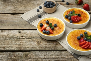 Delicious creme brulee with berries and mint in bowls on wooden table. Space for text