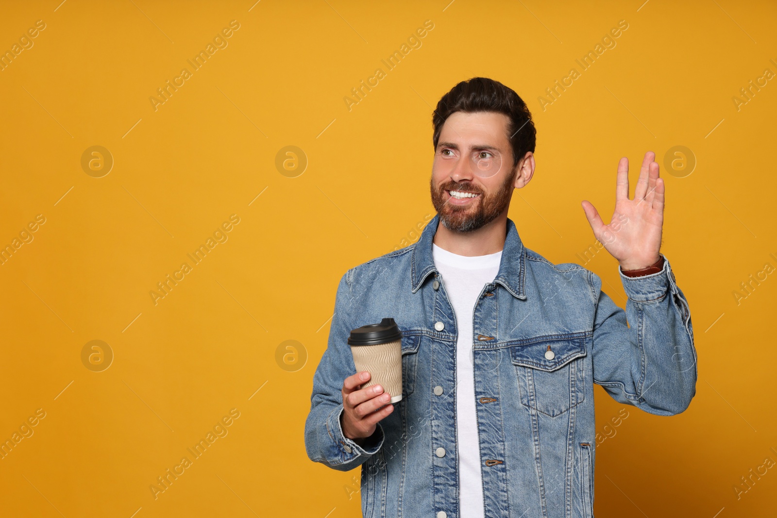Photo of Bearded man with paper cup of drink and open hand on orange background. Space for text
