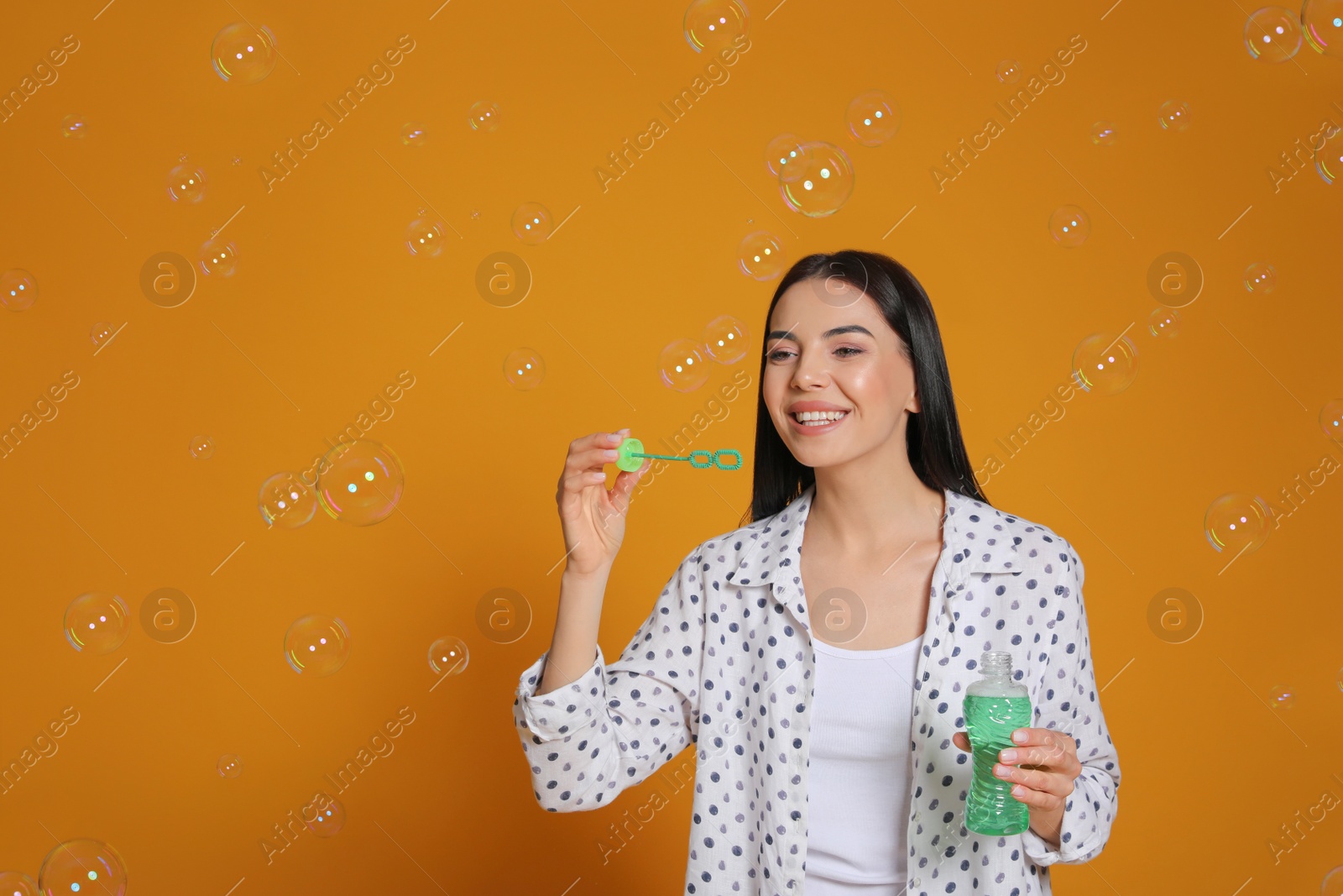 Photo of Young woman blowing soap bubbles on yellow background