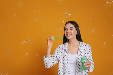 Young woman blowing soap bubbles on yellow background