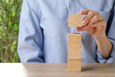 Photo of Woman stacking wooden cubes at table, closeup and space for text. Management concept