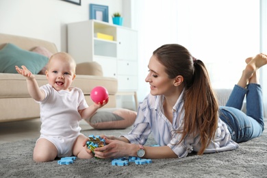 Happy mother playing with little baby on floor indoors