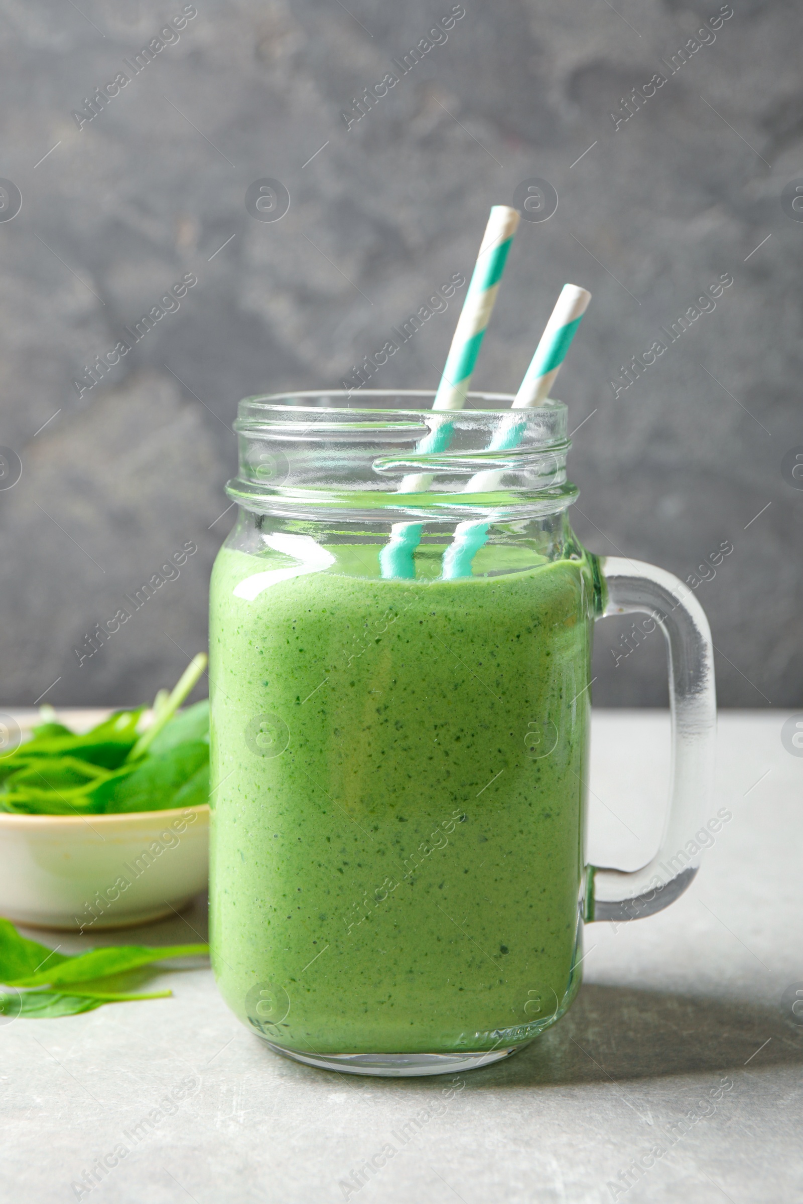 Photo of Mason jar of healthy green smoothie with fresh spinach on grey table