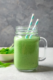 Photo of Mason jar of healthy green smoothie with fresh spinach on grey table