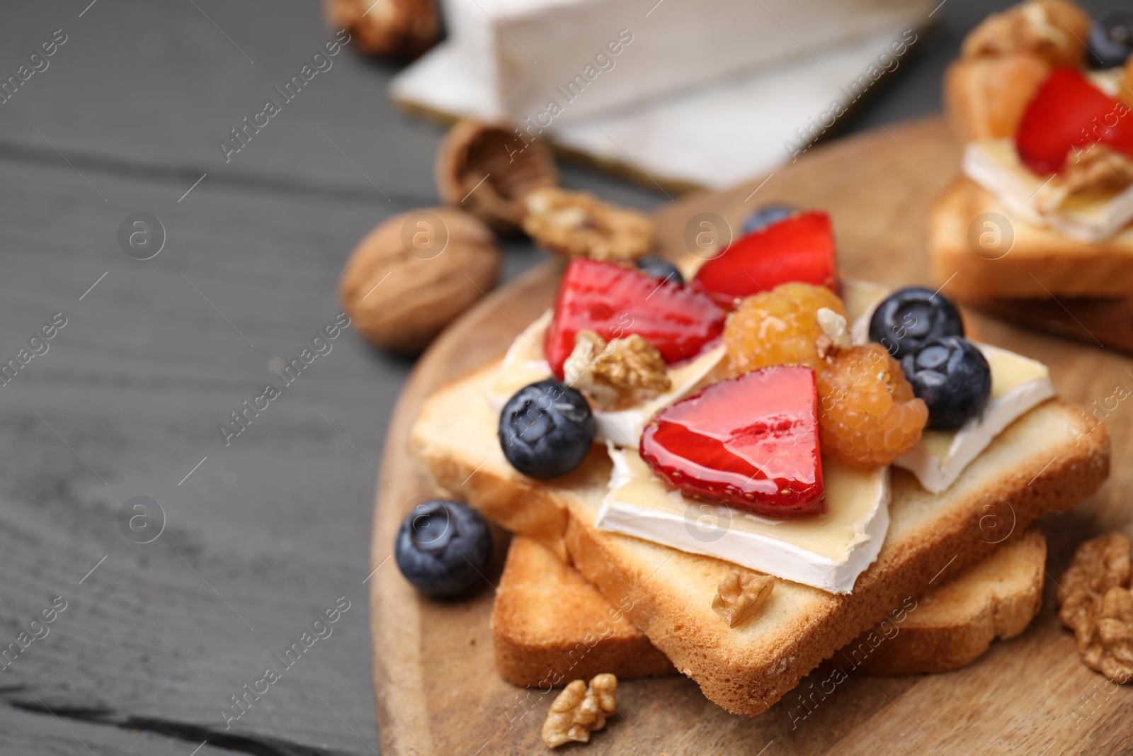 Photo of Tasty sandwich with brie cheese, fresh berries and walnuts on grey wooden table, closeup. Space for text