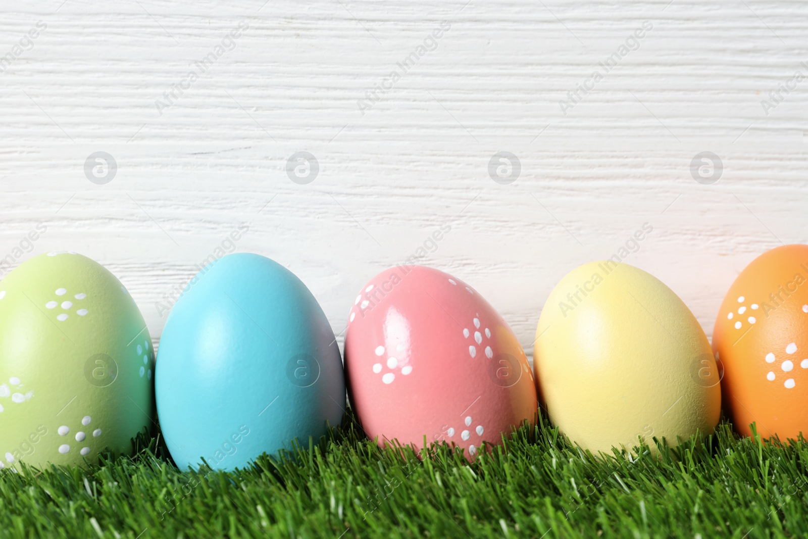 Photo of Colorful painted Easter eggs on green grass against wooden background, space for text