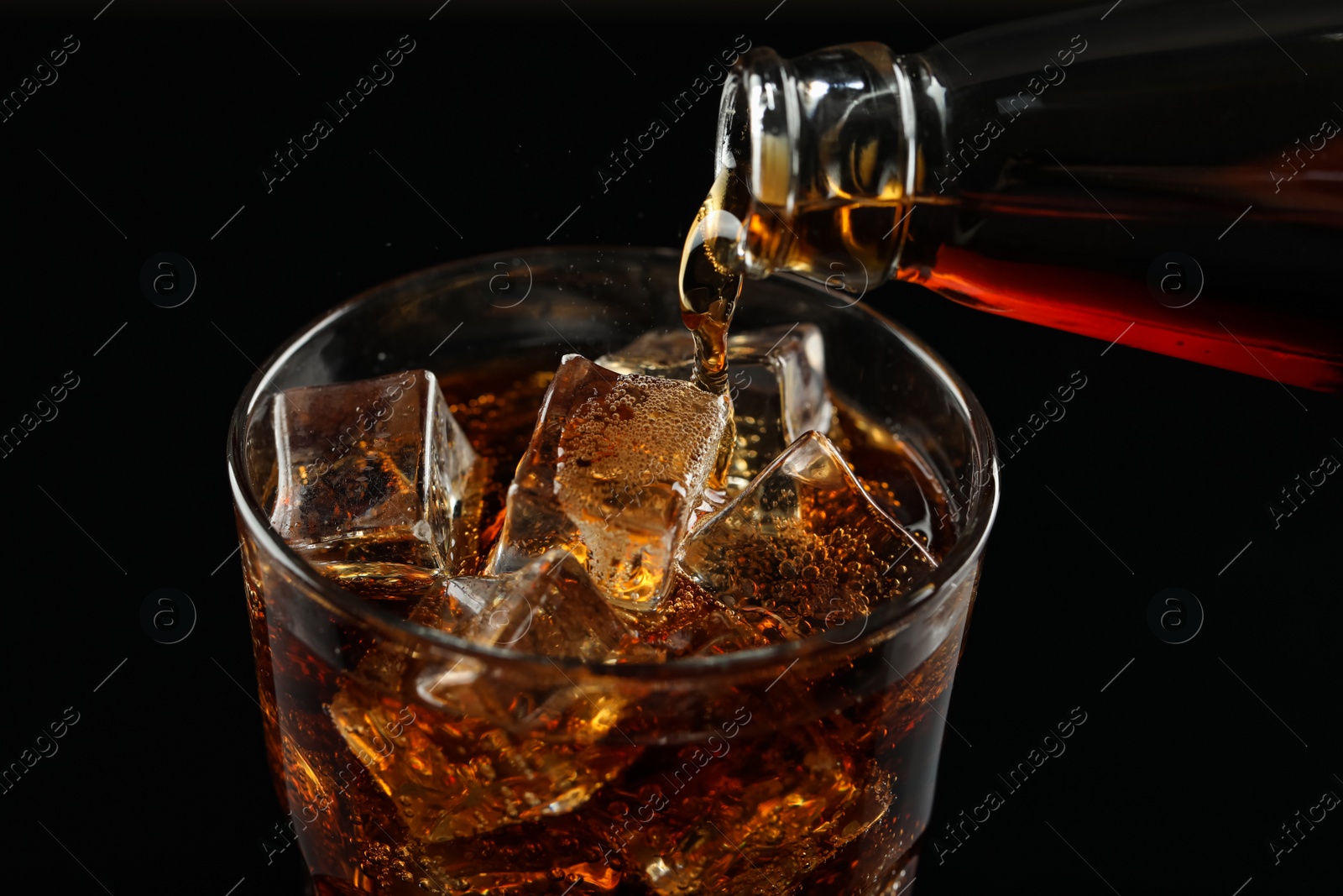 Photo of Pouring refreshing soda water from bottle into glass on black background, closeup