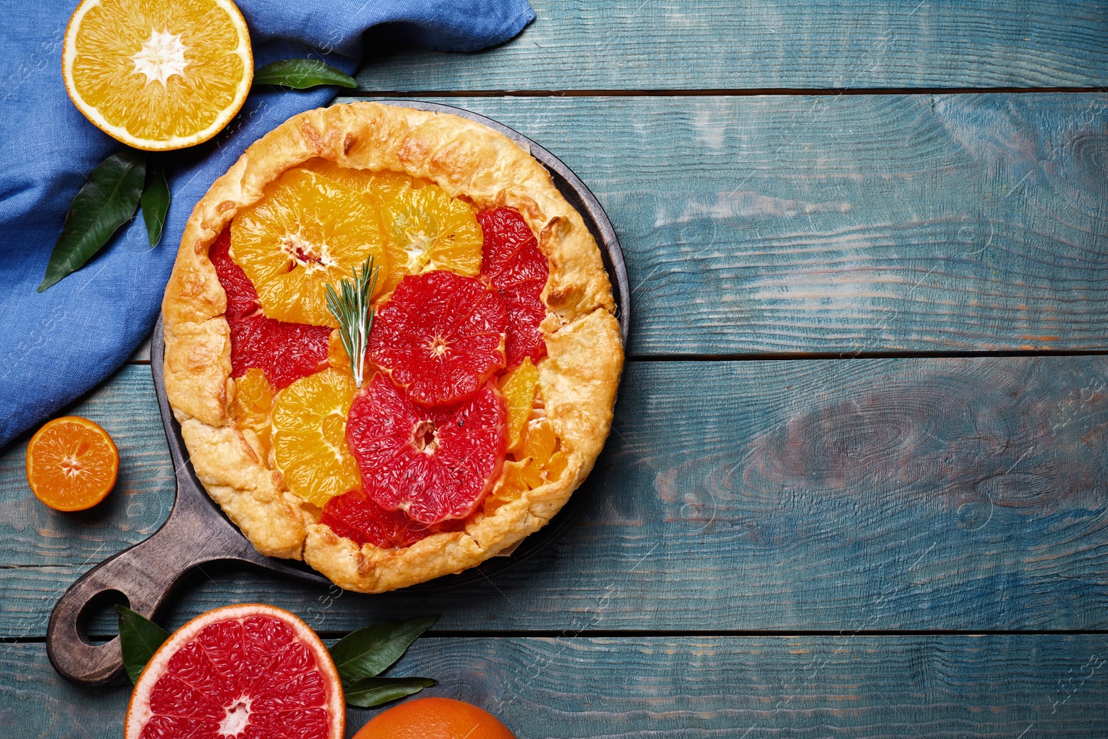 Photo of Delicious galette with citrus fruits and rosemary on blue wooden table, flat lay. Space for text