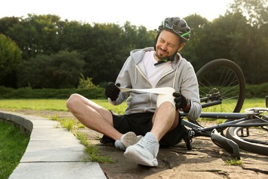 Photo of Man applying bandage onto his knee near bicycle outdoors