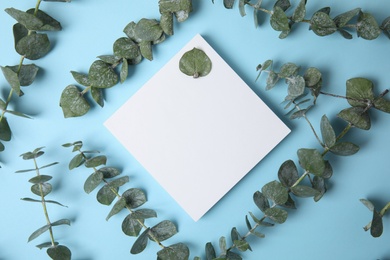 Fresh eucalyptus leaves and blank card with space for design on color background, top view