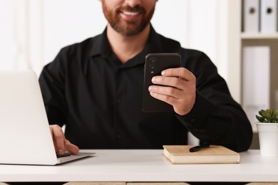 Photo of Smiling man using smartphone at table in office, closeup