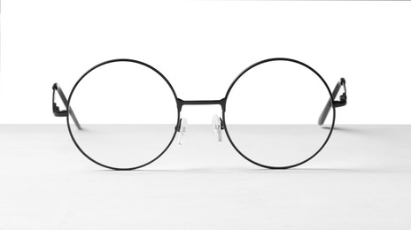 Photo of Round glasses with metal frame on table against white background