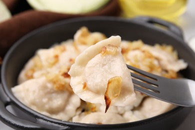 Photo of Fork with delicious dumpling (varenyk) and fried onions over plate, closeup