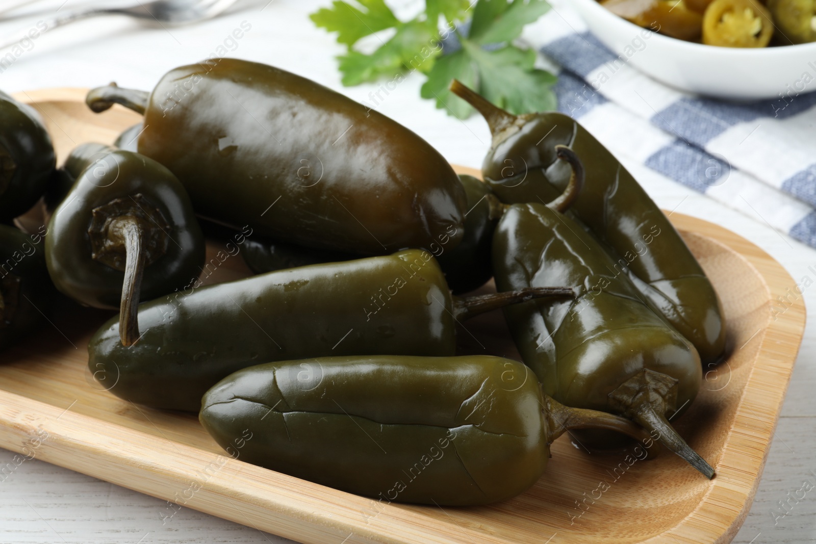 Photo of Wooden tray with pickled green jalapeno peppers on white table, closeup