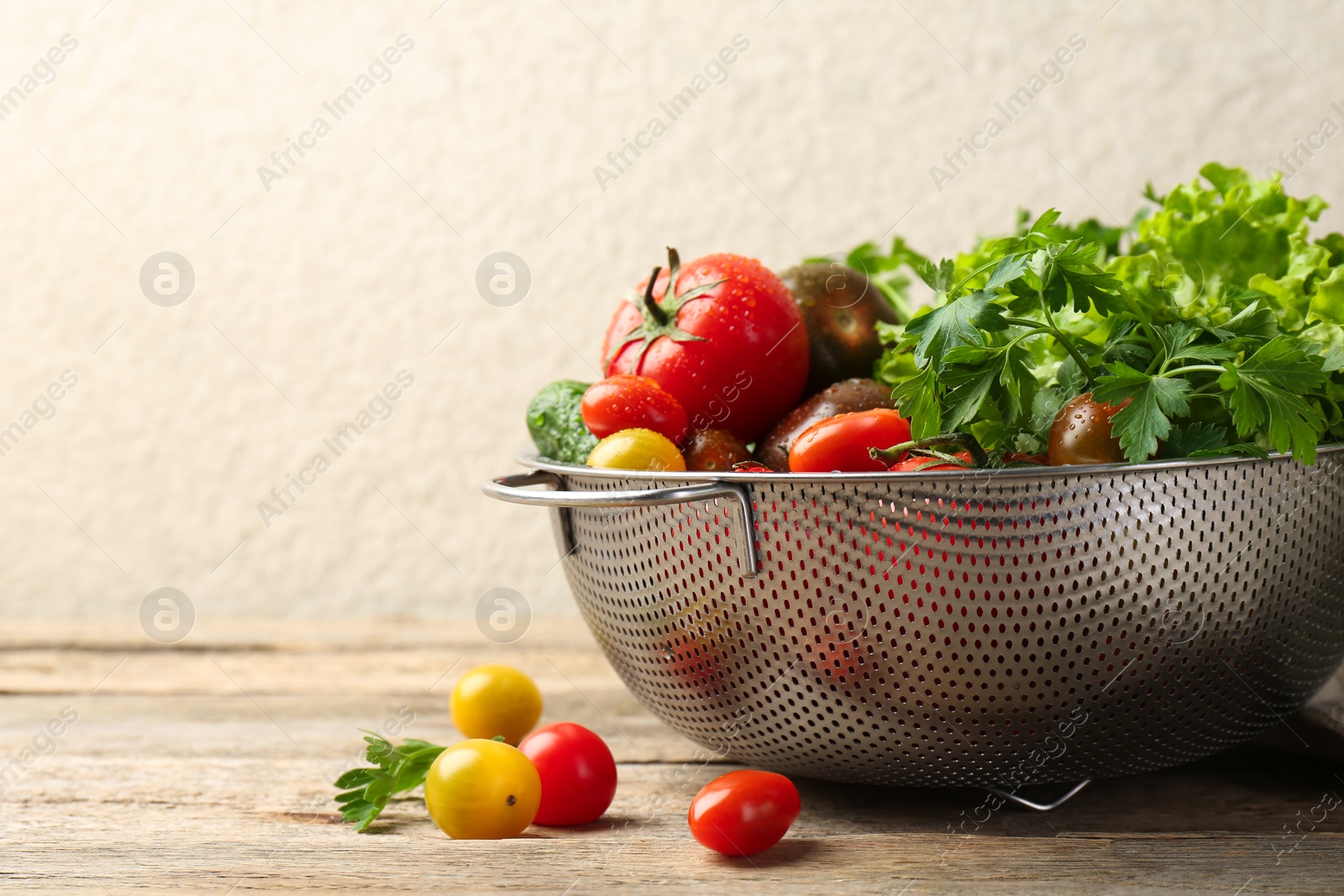 Photo of Wet vegetables in colander on wooden table, closeup. Space for text