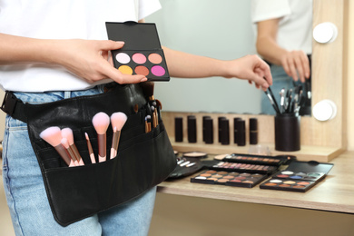 Professional makeup artist with eyeshadow palette near wooden table indoors, closeup